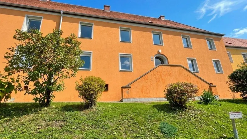 Mehrfamilienhaus mit leuchtend oranger Fassade und grüner Umgebung unter blauem Himmel.