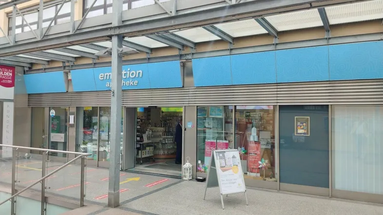 Eingangsbereich einer Apotheke mit Rampe und Schaufenstern in einem Geschäftszentrum.