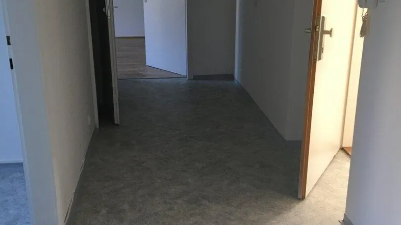 Heller Flur mit mehreren Türen und grauem Bodenbelag, der zu verschiedenen Räumen führt.