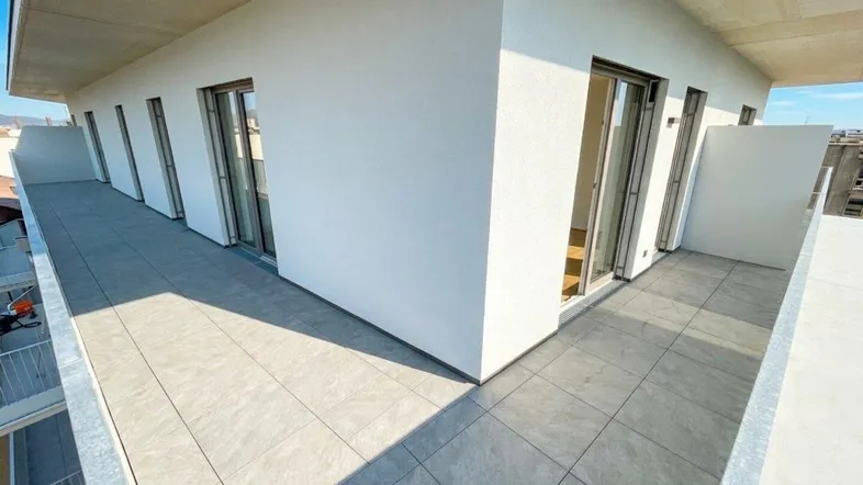 Lange, geflieste Terrasse mit weißer Brüstung und Zugang zu mehreren Räumen.