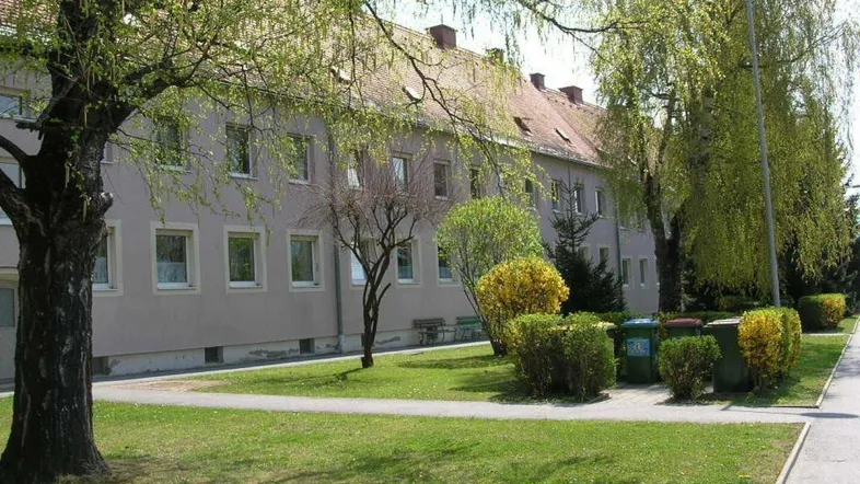 Mehrfamilienhaus mit gepflegter Grünfläche und Bäumen in einer ruhigen Wohngegend.