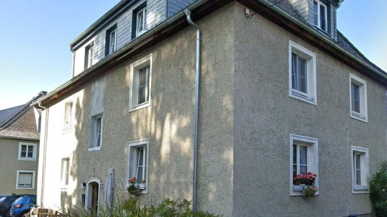 Mehrfamilienhaus mit Putzfassade und Schieferdach in einer ruhigen Wohngegend.