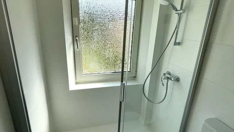Moderne Duschkabine mit Glasabtrennung und Fenster, Teil eines Badezimmers.