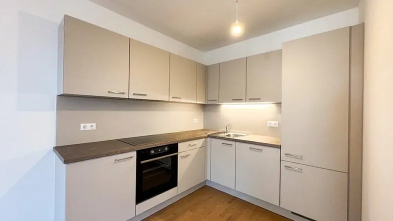 Moderne Einbauküche in hellem Beige mit dunkler Arbeitsplatte und Holzboden, ausgestattet mit Backofen und Kochfeld.