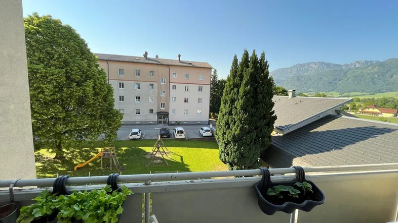 Blick vom Balkon auf die grüne Umgebung mit Spielplatz und Bergpanorama.