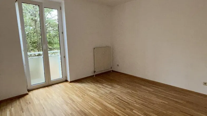 Heller, leerer Raum mit Parkettboden und Zugang zu einem kleinen Balkon oder einer französischen Balkontür.