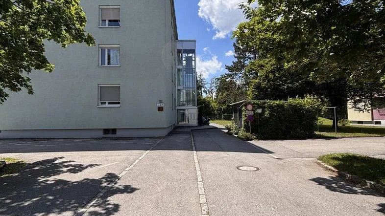 Außenansicht eines Wohngebäudes mit modernem Glasaufzug und umliegender Grünfläche.
