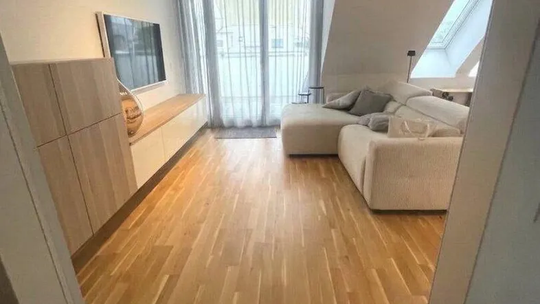 Helles Wohnzimmer mit modernem Sofa, Holzboden und Zugang zu einem Balkon, ergänzt durch Dachfenster.
