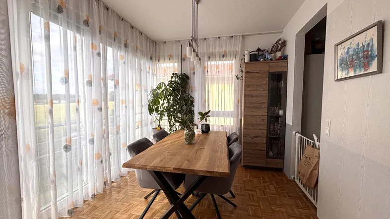 Heller Essbereich mit Holztisch, modernen Stühlen und großen Fenstern mit Blick ins Grüne.