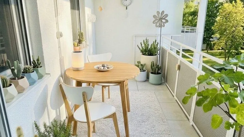 Heller Balkon mit Holztisch, Stühlen und vielen Pflanzen, ideal für entspannte Stunden im Freien.