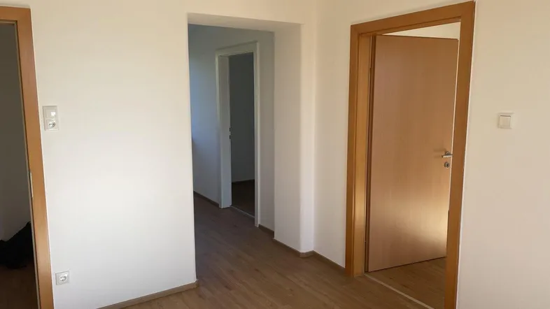Heller Flur mit Holztüren und Laminatboden, der zu verschiedenen Räumen führt.