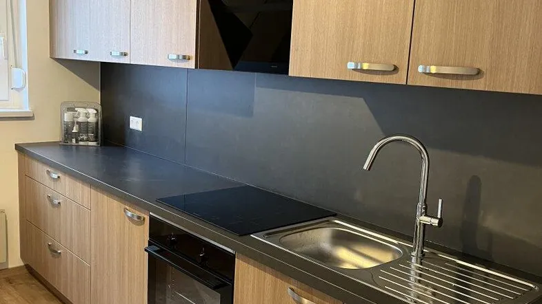 Moderne Küche mit hellen Holzfronten, dunkler Arbeitsplatte, integriertem Backofen und Induktionskochfeld.