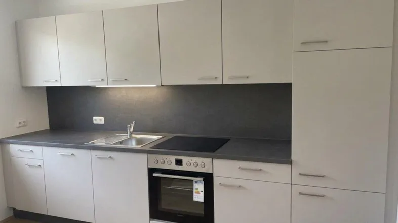 Moderne Einbauküche in hellem Grau mit dunkler Arbeitsplatte, integriertem Backofen und Induktionskochfeld.