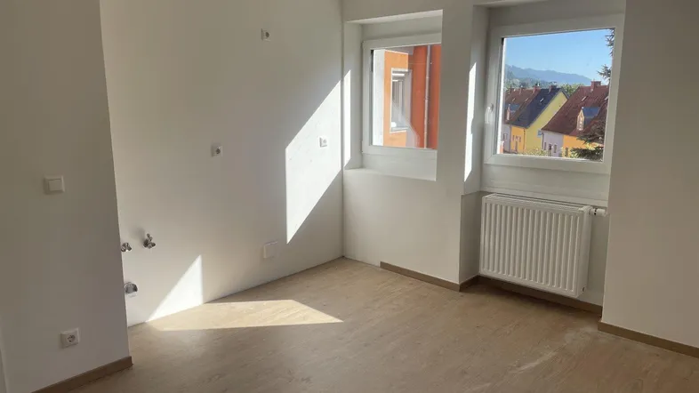 Helles Zimmer mit Laminatboden, Heizkörper und Blick auf die umliegende Landschaft.