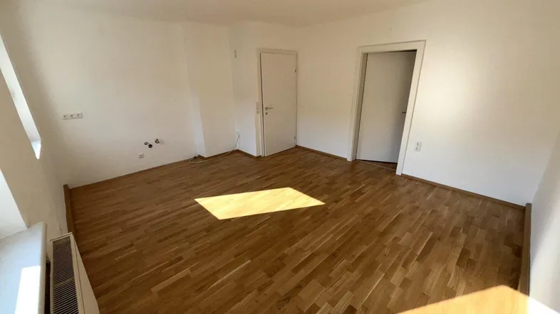 Helles, leeres Zimmer mit Parkettboden und Heizkörper, bereit zur individuellen Gestaltung.