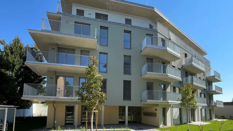 Modernes Mehrfamilienhaus mit mehreren Balkonen und gepflegter Außenanlage unter blauem Himmel.