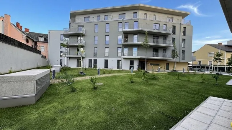 Modernes Mehrfamilienhaus mit Balkonen und gepflegter Grünfläche im Vordergrund unter blauem Himmel.