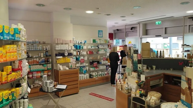 Innenansicht einer Apotheke mit Regalen voller Produkte und Kunden im Verkaufsbereich.