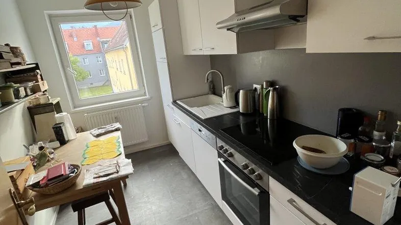 Helle Küche mit weißen Schränken, schwarzer Arbeitsplatte und integrierten Geräten, inklusive Essbereich am Fenster.