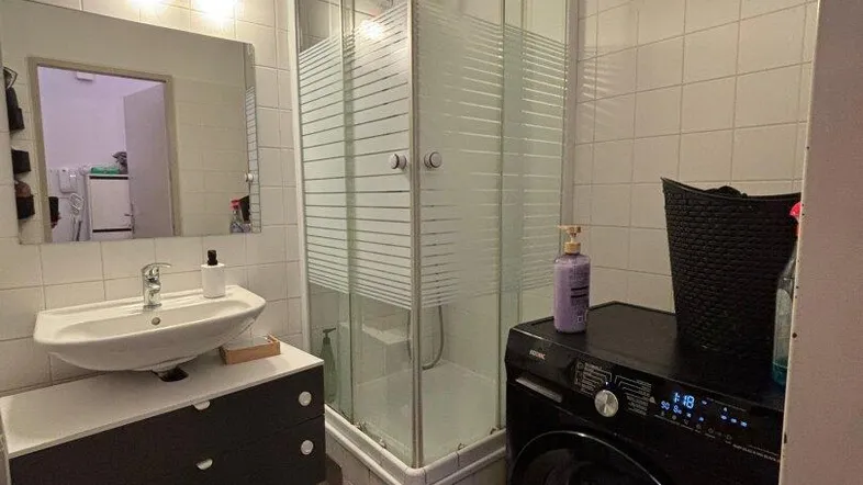 Funktionales Badezimmer mit Duschkabine, Waschbecken und integrierter Waschmaschine.
