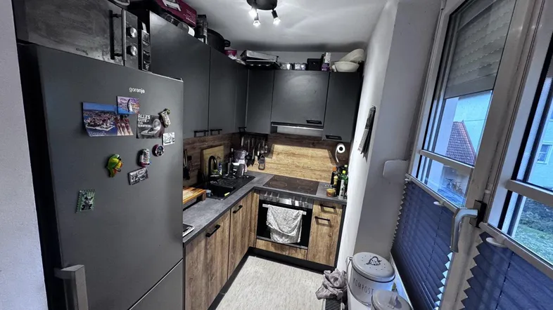 Moderne Küche mit dunklen Schränken, Holzoptik-Arbeitsplatten und integriertem Kühlschrank, hell beleuchtet durch Fenster.