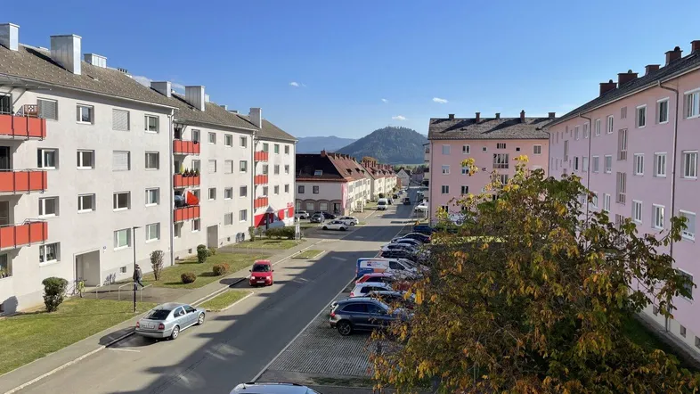 Blick auf die Wohnanlage mit geparkten Autos und Bergen im Hintergrund unter blauem Himmel.