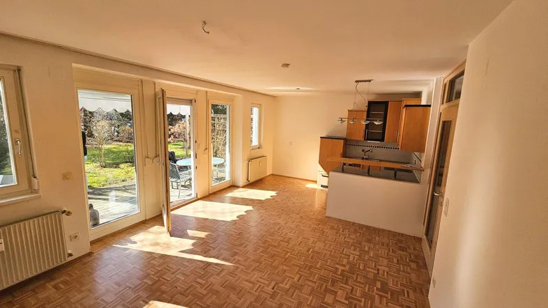 Helles Wohnzimmer mit integrierter Küche, Parkettboden und Zugang zur sonnigen Terrasse.