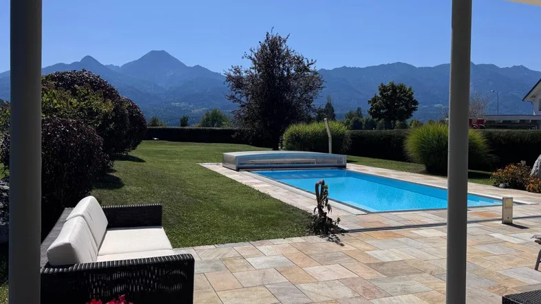 Große Terrasse mit Pool, Gartenmöbeln und beeindruckendem Bergblick unter blauem Himmel.