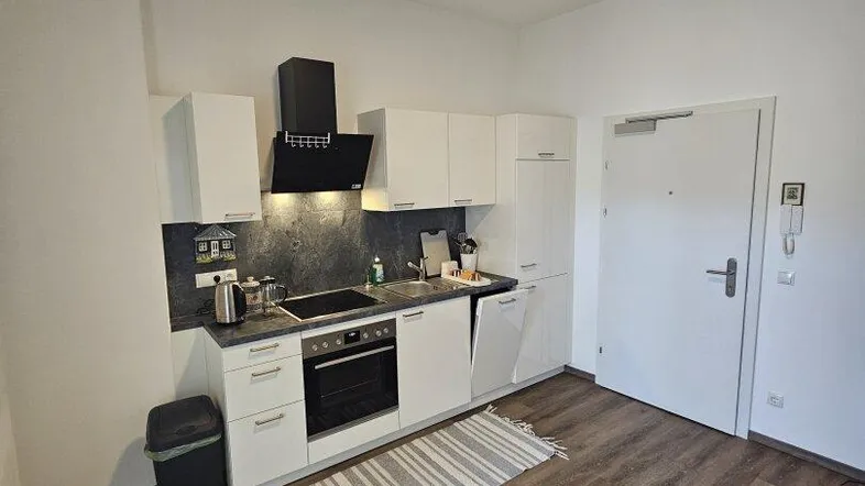 Kompakte Küche mit weißen Schränken, dunkler Arbeitsplatte und Laminatboden.