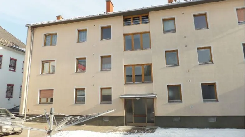 Fassade eines Mehrfamilienhauses mit mehreren Fenstern und einem Eingangsbereich im Erdgeschoss, umgeben von Schnee.