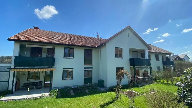 Mehrfamilienhaus mit gepflegtem Garten, Balkonen und Terrassen unter blauem Himmel.