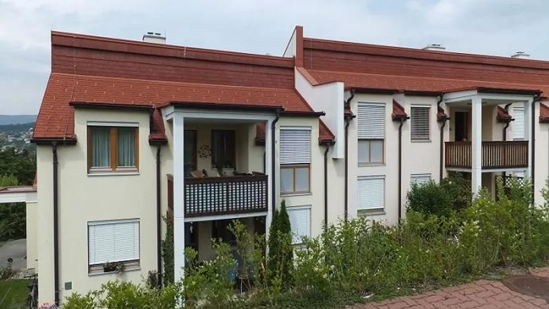 Mehrfamilienhaus mit rotem Ziegeldach und Balkonen in ländlicher Umgebung.