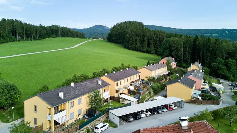 Luftaufnahme von Reihenhäusern mit Carports und grüner Landschaft im Hintergrund.