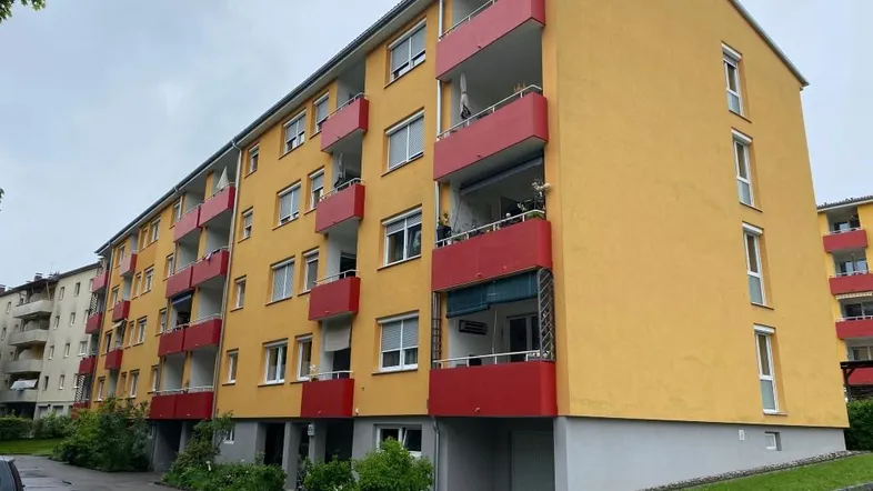 Mehrstöckiges Wohngebäude mit gelber Fassade und roten Balkonen unter bewölktem Himmel.