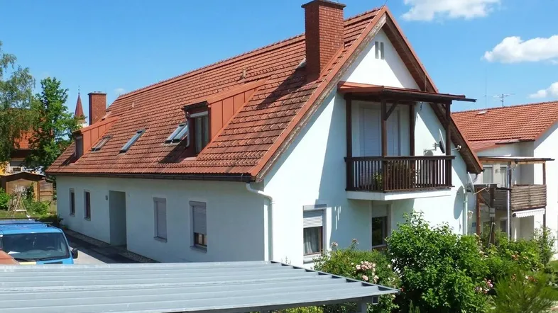 Gepflegtes Einfamilienhaus mit rotem Ziegeldach, weißer Fassade und kleinem Balkon.