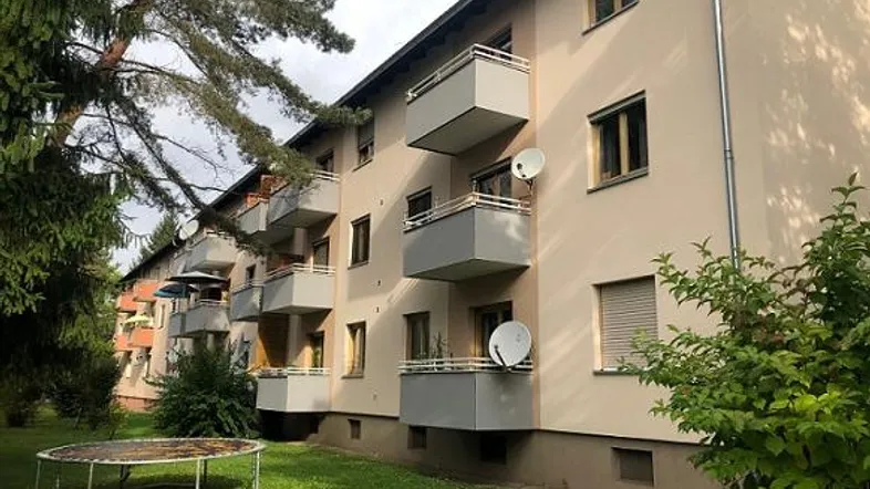 Mehrfamilienhaus mit mehreren Balkonen und einem gepflegten Gartenbereich inklusive Trampolin.