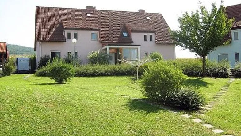 Einfamilienhaus mit großem, gepflegtem Garten und Rasenfläche, umgeben von grüner Landschaft.