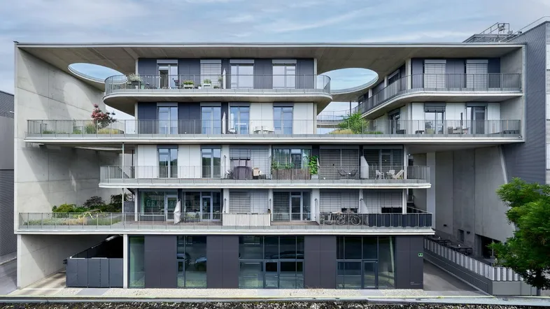 Moderne Wohnfassade mit geschwungenen Balkonen und großen Fensterfronten aus Beton und Glas.