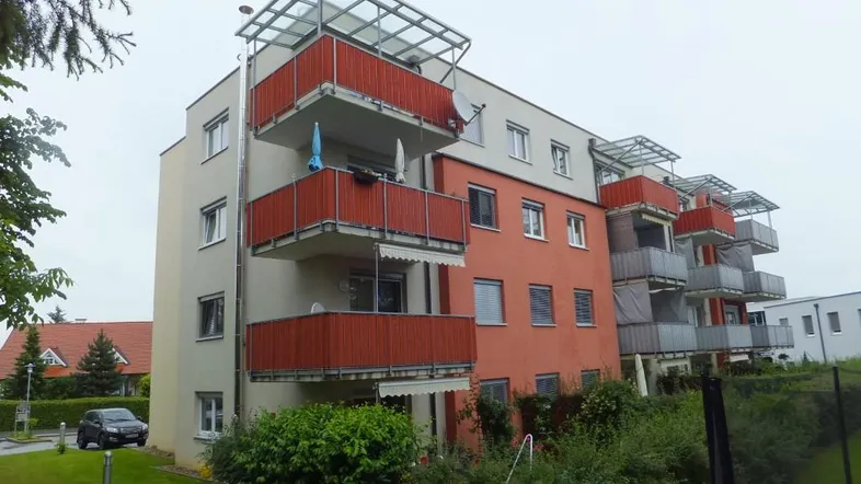 Modernes Mehrfamilienhaus mit mehreren Balkonen und einer Kombination aus beigen und roten Fassaden.