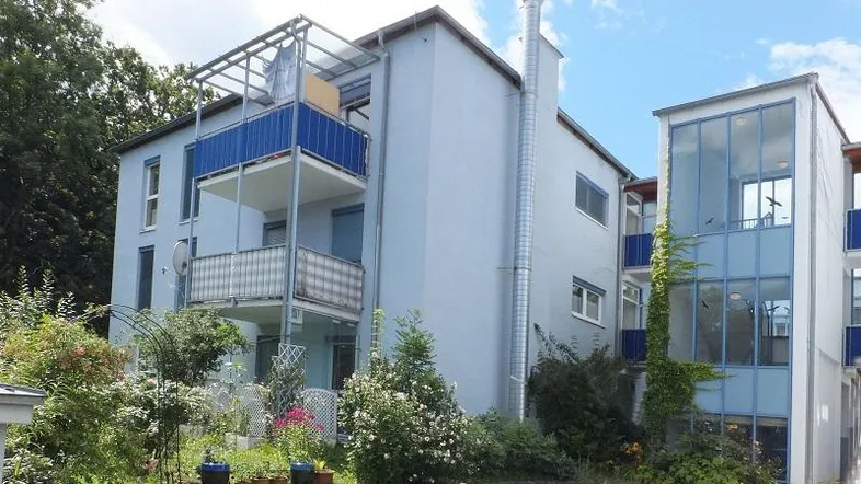 Mehrfamilienhaus mit hellblauer Fassade, Balkonen und einem gepflegten Vorgartenbereich.