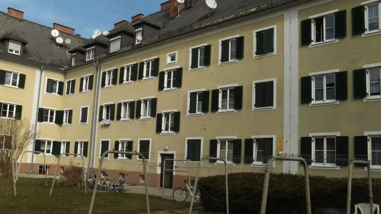 Mehrfamilienhaus mit gelber Fassade, grünen Fensterläden und einem Spielplatz im Innenhof.