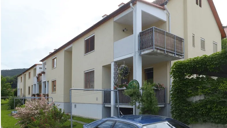 Mehrfamilienhaus mit beiger Fassade, mehreren Balkonen und grüner Umgebung.
