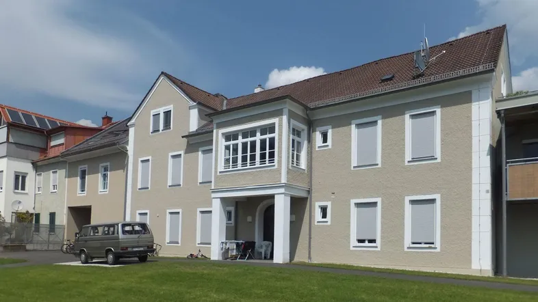 Mehrfamilienhaus mit heller Fassade, Rollläden und einem gepflegten Vorgarten.