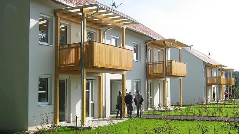 Moderne Reihenhäuser mit Balkonen und Terrassen, umgeben von einer gepflegten Grünfläche.