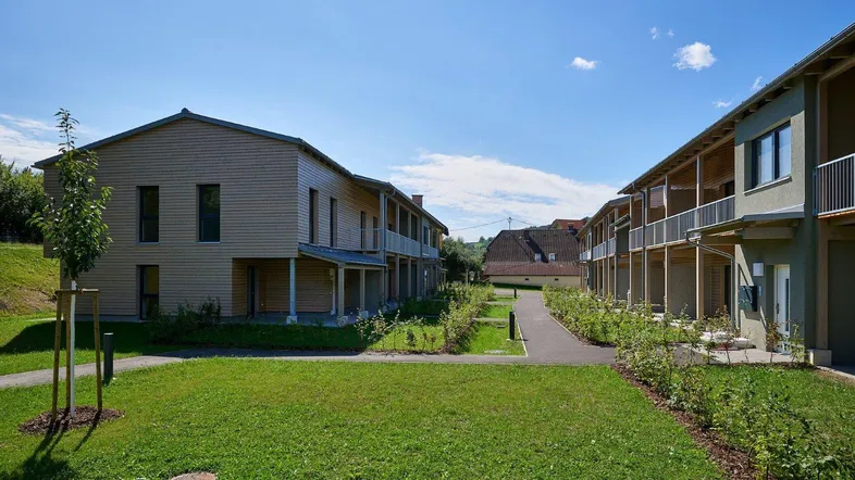 Moderne Wohngebäude mit Holzfassaden und gepflegten Grünflächen unter blauem Himmel.