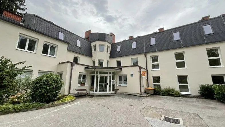 Ansicht eines gepflegten Mehrfamilienhauses mit Eingangsbereich und Schieferdach unter bewölktem Himmel.