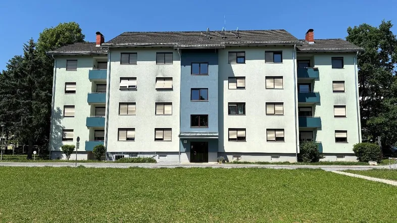 Mehrfamilienhaus mit hellgrüner Fassade und blauen Akzenten, umgeben von Grünflächen.