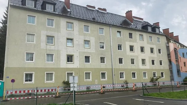 Mehrfamilienhaus mit heller Fassade und Satteldach in einer grünen Umgebung.