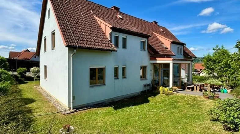 Großzügiges Einfamilienhaus mit Satteldach und weitläufigem Gartenbereich unter blauem Himmel.
