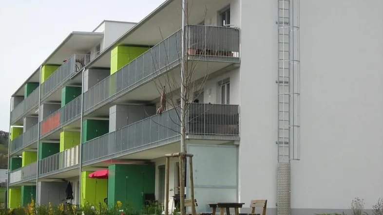 Modernes Mehrfamilienhaus mit farbigen Balkonen und gepflegter Grünfläche im Vordergrund.